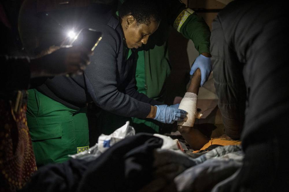 Ntombikayisi Joko (2nd L), 43, an Intermediate Life Support paramedic with the Southern Division paramedic at Mitchells Plain EMS base, applies bandages at the dwelling of a head trauma and stab wound patient while on night shift duty in the Philippi township, Cape Town, within the broader Cape Flats area, on April 15, 2025. Cape Town’s Emergency Medical Services (EMS) refuses to allow its medical crews to move without security cover when they operate in Red Zones. (Photo by MARCO LONGARI/AFP)